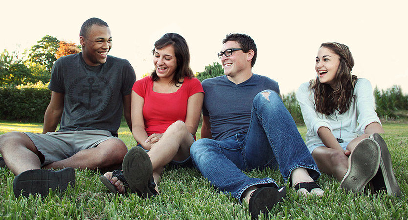 smiling-women-and-men-sitting-on-green-grass